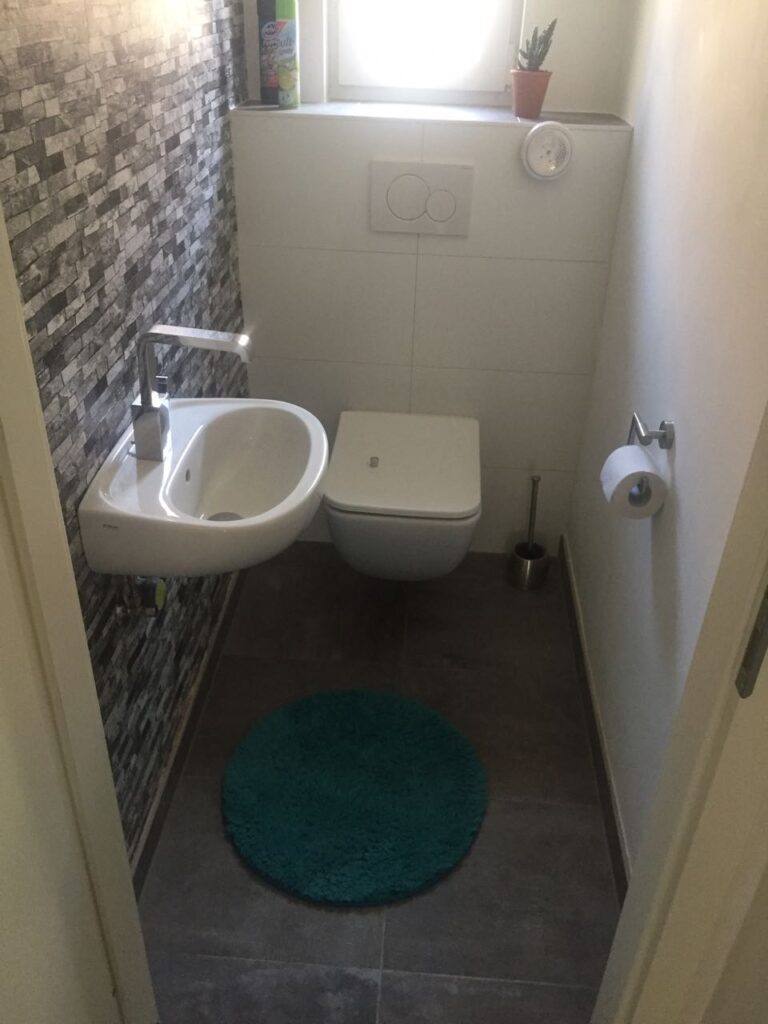 Kleines Gäste-WC nach Badsanierung mit wandhängendem WC, kompaktem Waschtisch und Steinoptik-Fliesen