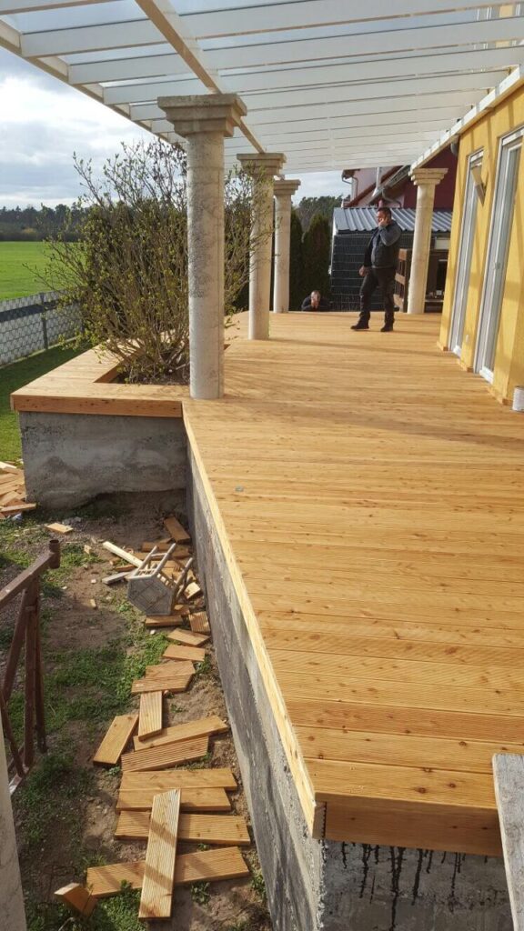 Neue Holzterrasse auf Betonunterbau mit Säulen und Handwerkern, fertige Bodenverlegung im Rahmen der Bausanierung